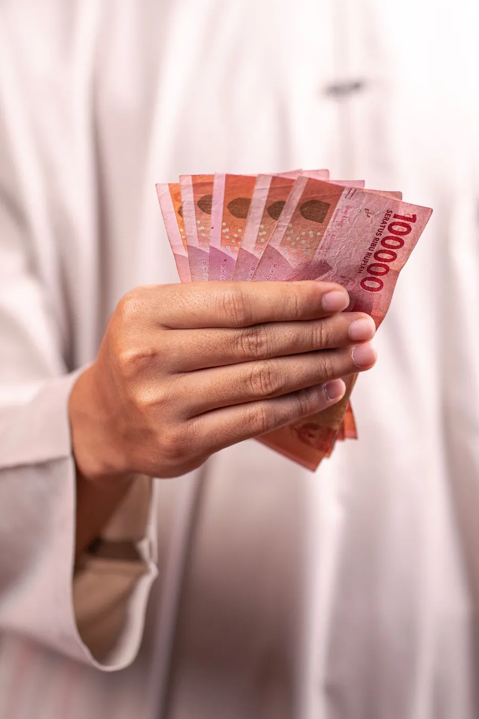 A hand holding Indonesian rupiah banknotes, representing sale proceeds before repatriation