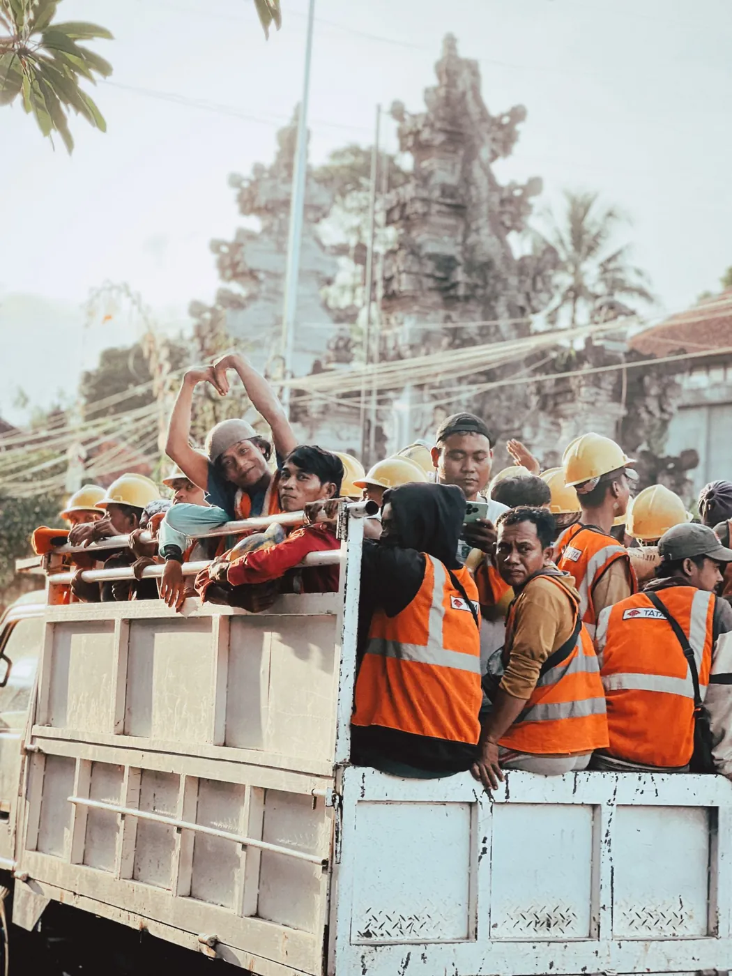 A Balinese construction crew in high-visibility vests, with a Hindu temple gate behind them