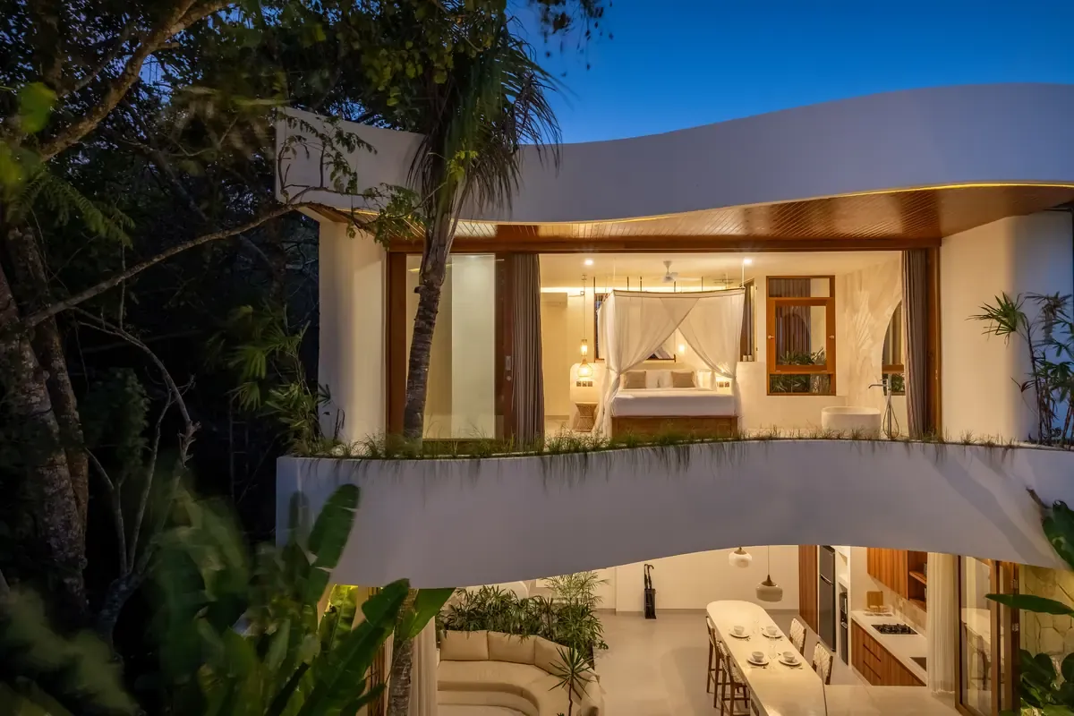 A Premier villa at dusk, lit from within, set into the jungle